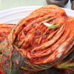 Whole napa cabbage kimchi coated in red pepper seasoning on a white plate