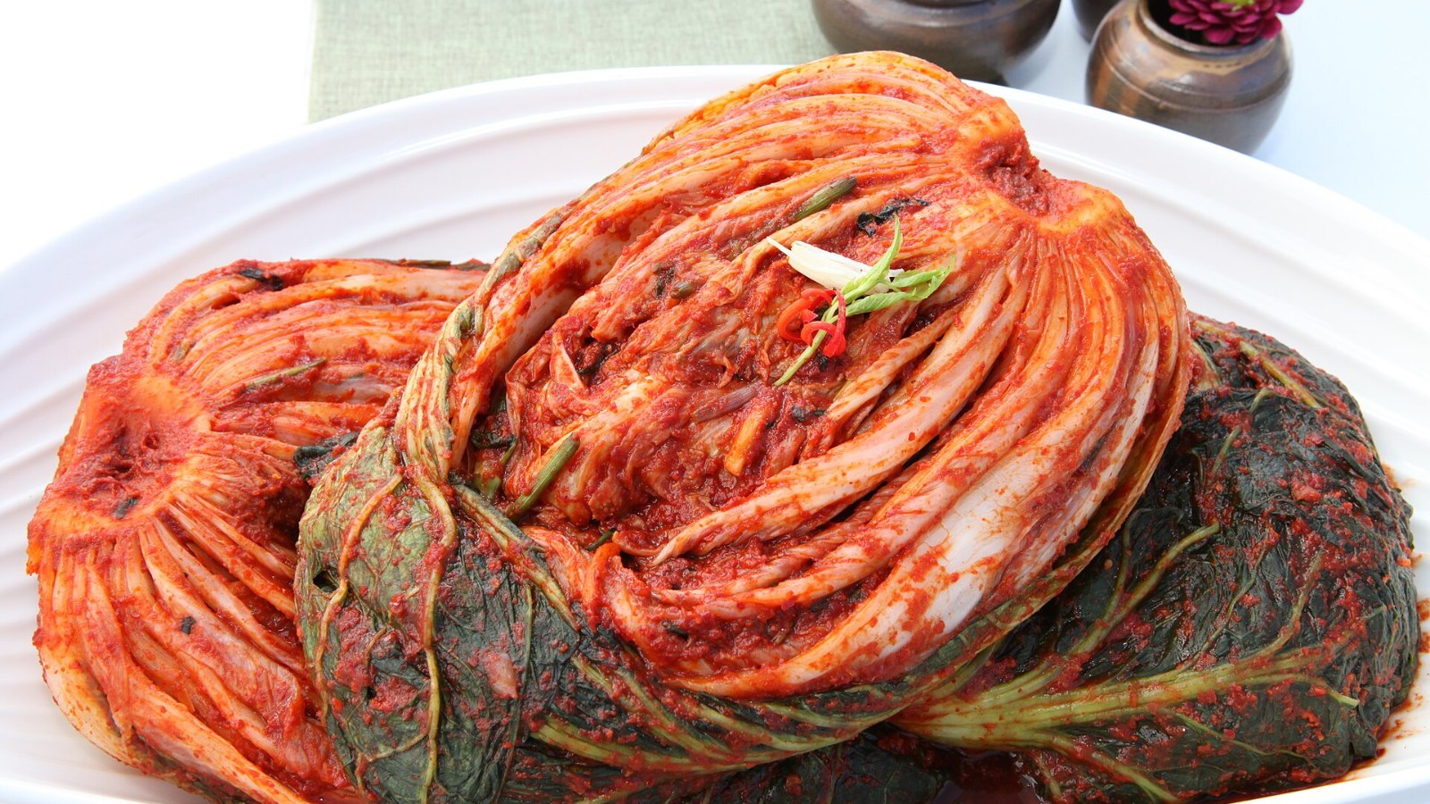 Whole napa cabbage kimchi coated in red pepper seasoning on a white plate