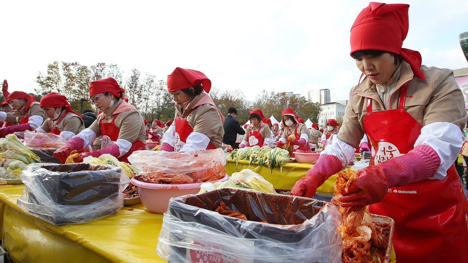 Volunteers in red aprons and caps seasoning cabbage together at the Seoul Kimchi Making and Sharing Festival