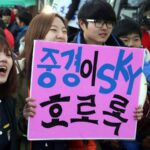 High school students in school uniforms cheering with handmade signs outside a Suneung test site in Seoul