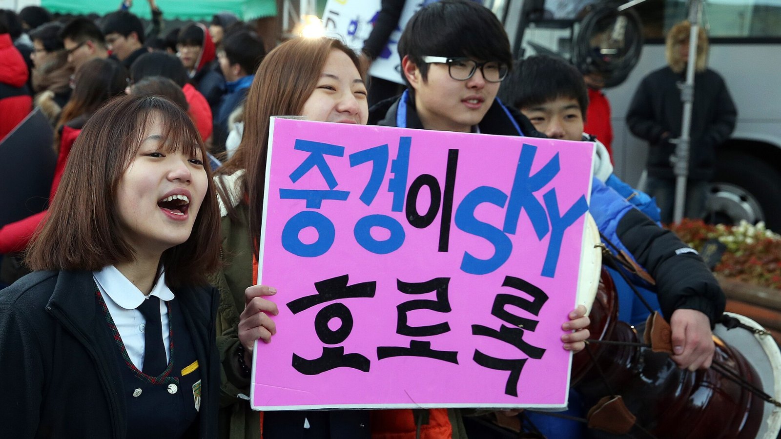 High school students in school uniforms cheering with handmade signs outside a Suneung test site in Seoul