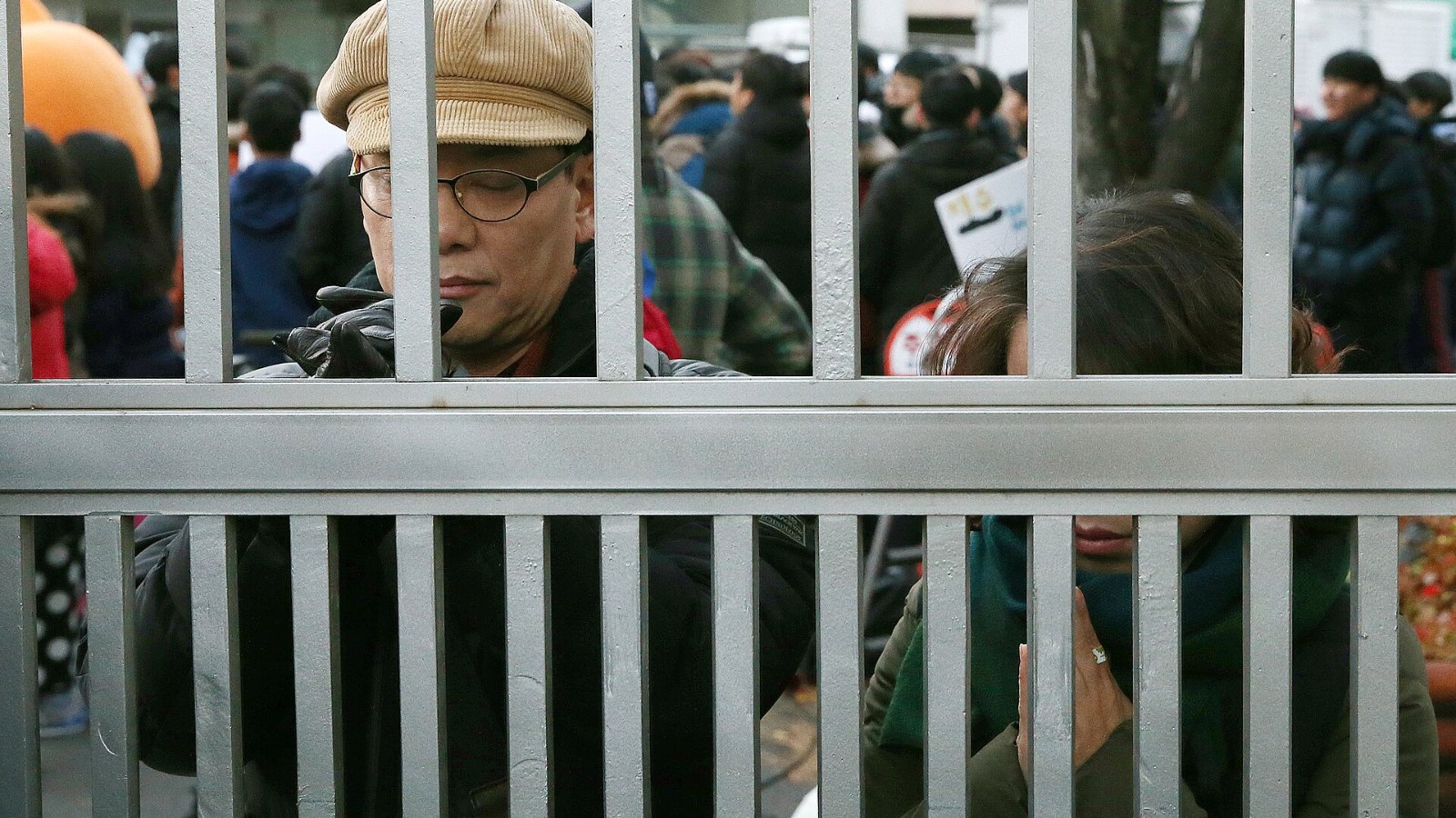 A parent praying at the closed gate of a Suneung test site after the exam began